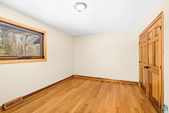 empty room featuring light wood-type flooring, visible vents, baseboards, and a textured ceiling