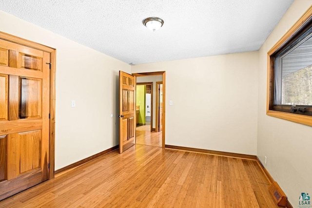 unfurnished room featuring visible vents, baseboards, light wood-style floors, and a textured ceiling