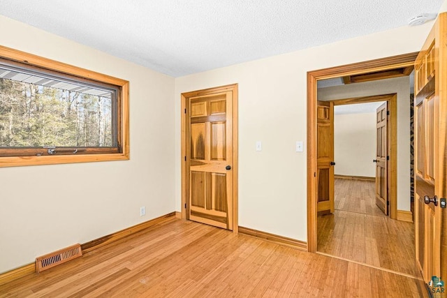 unfurnished bedroom with visible vents, baseboards, light wood-style floors, and a textured ceiling