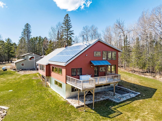 back of property featuring roof mounted solar panels, a lawn, a wooden deck, and metal roof