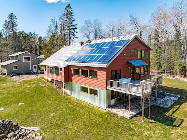 back of property featuring roof mounted solar panels, a yard, a wooden deck, metal roof, and a chimney