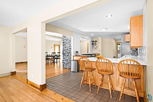 kitchen with a peninsula, freestanding refrigerator, wood finished floors, a sink, and a breakfast bar