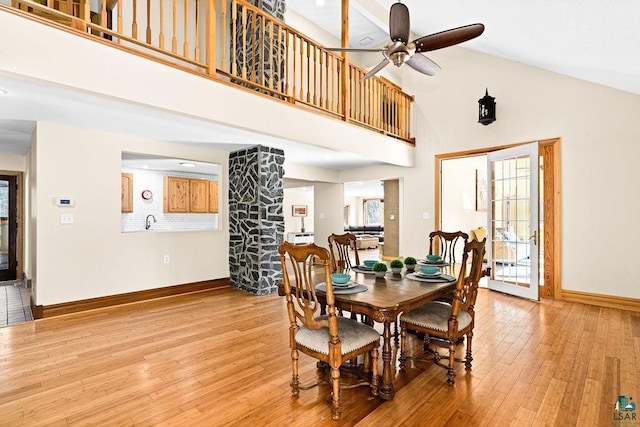 dining room with ceiling fan, high vaulted ceiling, baseboards, and light wood-type flooring