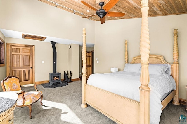 bedroom with a wood stove, wooden ceiling, carpet flooring, baseboards, and ceiling fan