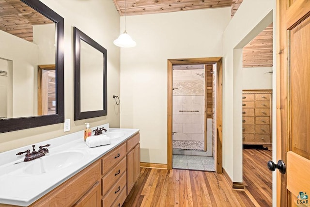 bathroom featuring hardwood / wood-style flooring, wooden ceiling, a tile shower, baseboards, and double vanity