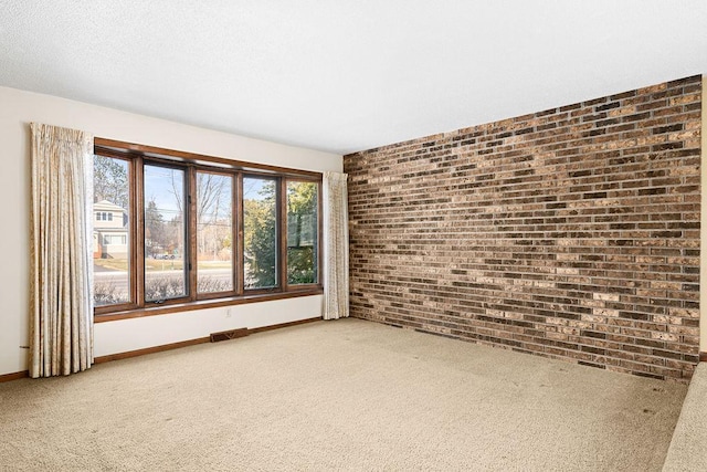 carpeted spare room with visible vents, baseboards, a textured ceiling, and brick wall