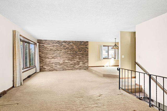 spare room with carpet flooring, brick wall, a textured ceiling, and baseboards