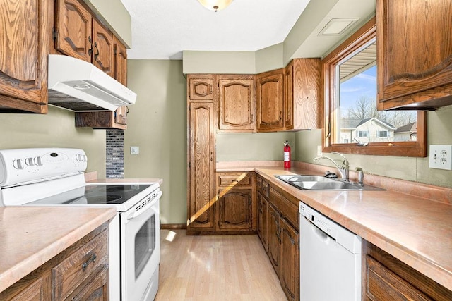 kitchen with white appliances, light wood-style flooring, a sink, under cabinet range hood, and brown cabinets