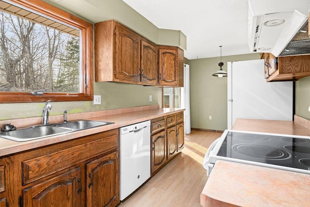 kitchen with white appliances, brown cabinetry, a sink, light countertops, and light wood-style floors