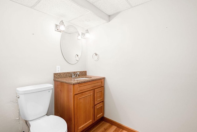 half bath with vanity, wood finished floors, baseboards, a paneled ceiling, and toilet