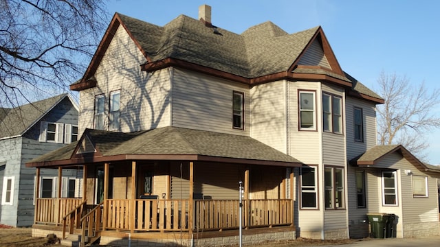 view of front of home with a porch, roof with shingles, and a chimney