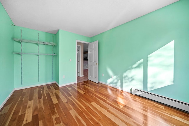 unfurnished bedroom featuring a baseboard radiator, baseboards, a closet, and wood finished floors