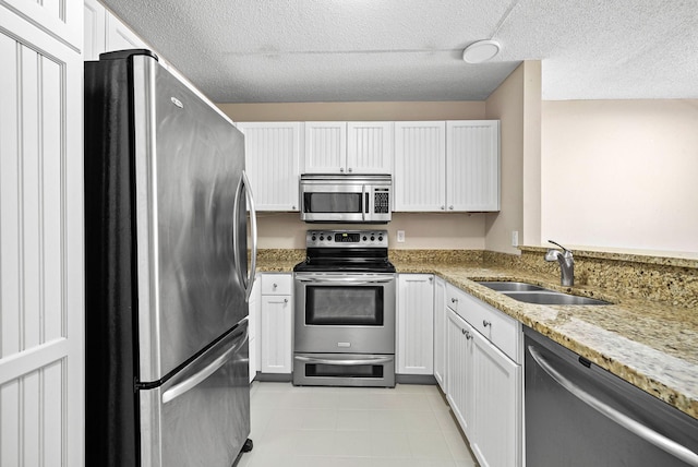 kitchen featuring light stone countertops, white cabinets, a textured ceiling, stainless steel appliances, and a sink