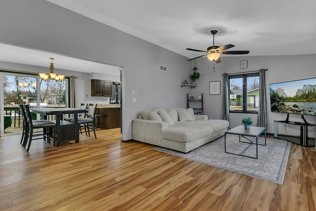 living room with light wood-type flooring, visible vents, ceiling fan with notable chandelier, and vaulted ceiling