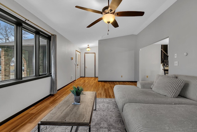 living area featuring baseboards, ceiling fan, stairs, lofted ceiling, and light wood-style floors