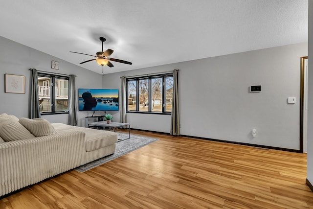 living area featuring baseboards, light wood-style flooring, a ceiling fan, and vaulted ceiling