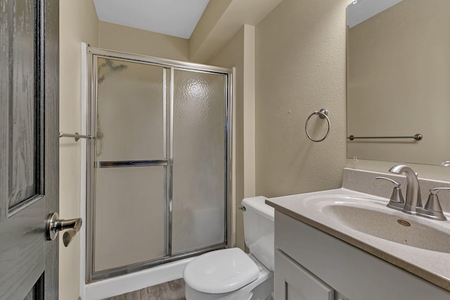 full bath featuring toilet, a stall shower, vanity, and a textured wall