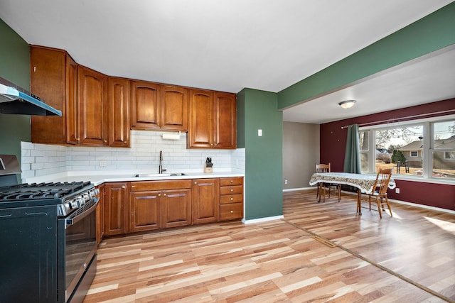 kitchen with brown cabinetry, stainless steel range with gas stovetop, light countertops, and a sink