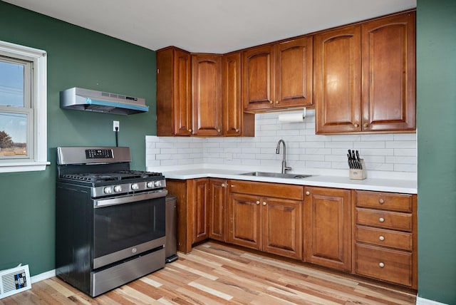 kitchen with brown cabinetry, visible vents, stainless steel gas range, a sink, and under cabinet range hood