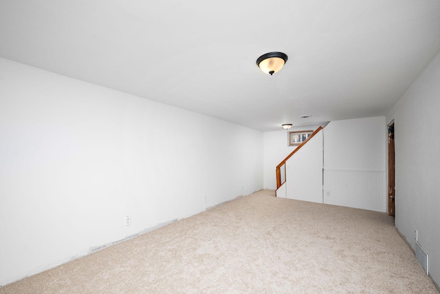 finished below grade area featuring stairs, carpet, visible vents, and wainscoting