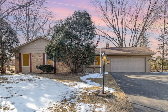 view of front facade with brick siding, an attached garage, a chimney, and driveway