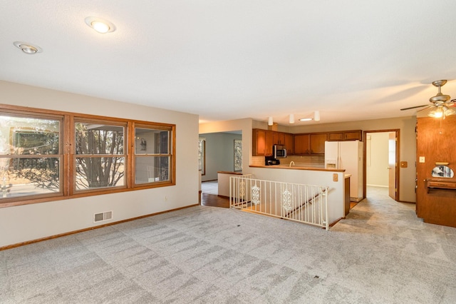 kitchen featuring visible vents, stainless steel microwave, light carpet, brown cabinets, and white fridge with ice dispenser