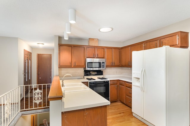 kitchen featuring brown cabinetry, a sink, white refrigerator with ice dispenser, gas range oven, and stainless steel microwave