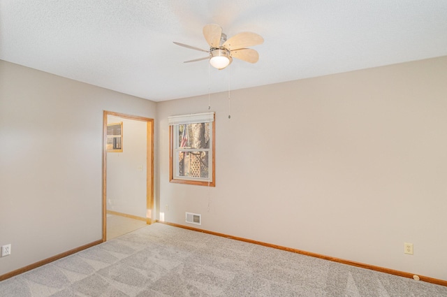 carpeted spare room with visible vents, baseboards, and a ceiling fan