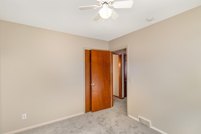 empty room with a ceiling fan, light colored carpet, visible vents, and baseboards