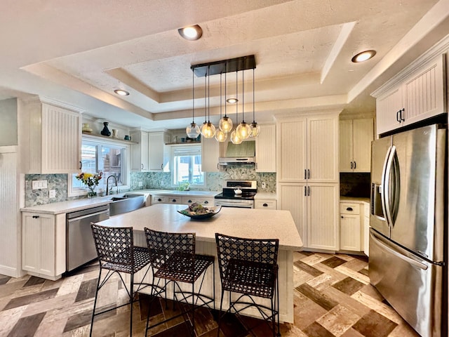 kitchen with backsplash, a breakfast bar area, light countertops, a tray ceiling, and stainless steel appliances