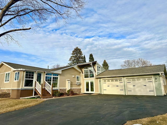 view of front facade with driveway, an attached garage, french doors, and roof with shingles