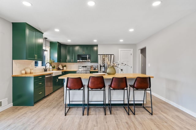 kitchen with light wood-type flooring, a breakfast bar, tasteful backsplash, stainless steel appliances, and green cabinetry