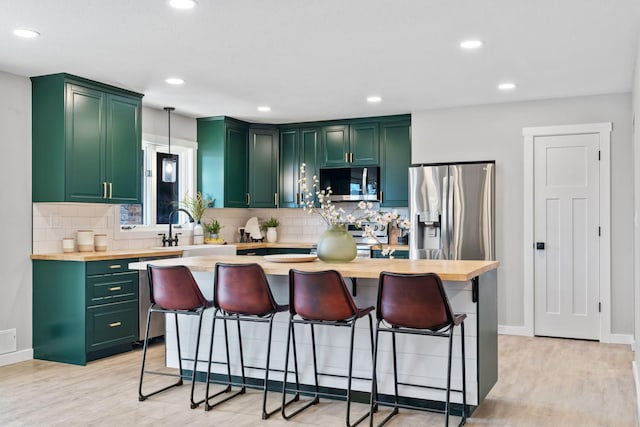 kitchen featuring light wood-style flooring, stainless steel appliances, green cabinets, and a sink