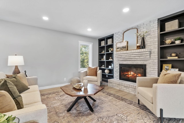 living room featuring built in shelves, baseboards, recessed lighting, a fireplace, and wood finished floors