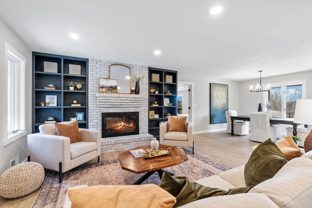 living room with built in shelves, wood finished floors, recessed lighting, an inviting chandelier, and a fireplace