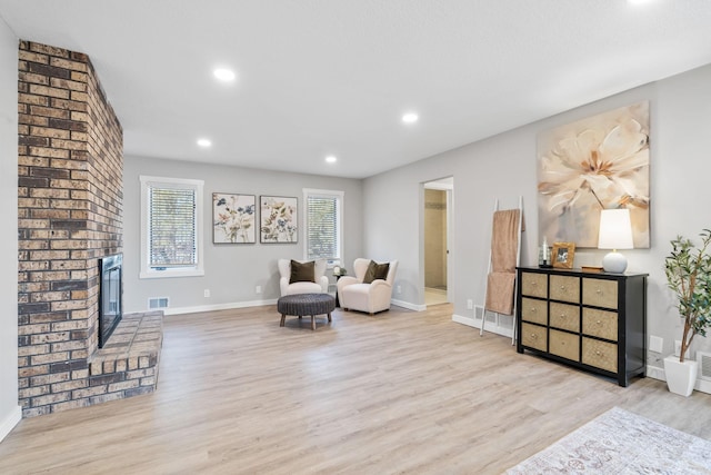 living area featuring a brick fireplace, wood finished floors, visible vents, and baseboards