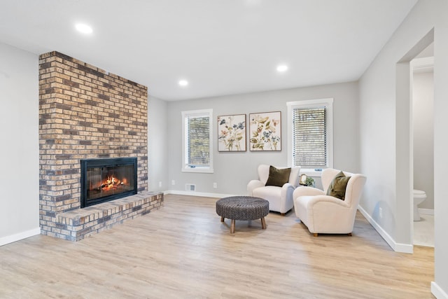 sitting room featuring visible vents, plenty of natural light, a brick fireplace, and wood finished floors