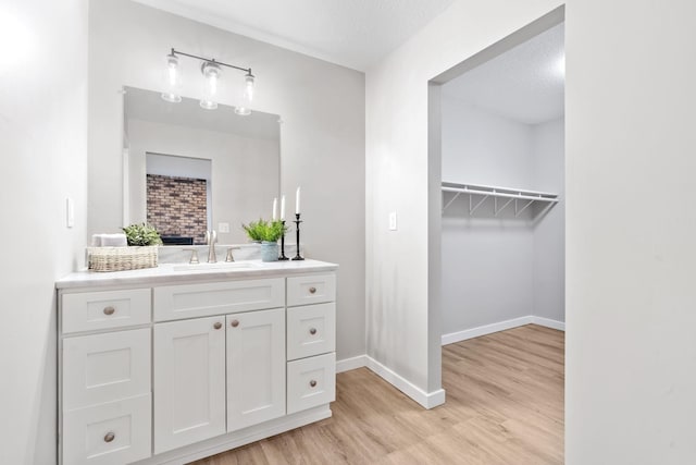 bathroom with vanity, wood finished floors, baseboards, a spacious closet, and a textured ceiling