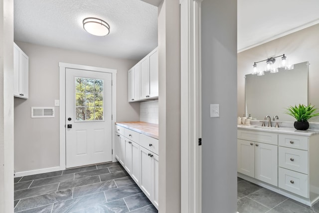 laundry room with a sink, visible vents, baseboards, and a textured ceiling