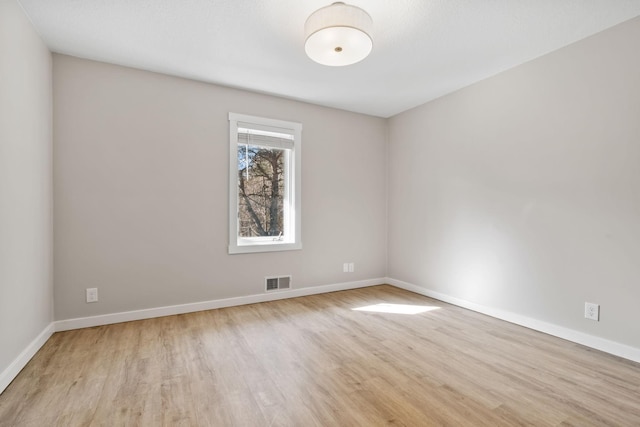 empty room with wood finished floors, visible vents, and baseboards