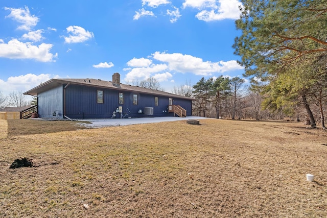 rear view of property with central AC unit, entry steps, a chimney, and a yard