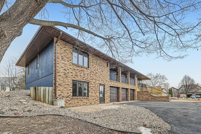 view of side of property with brick siding, an attached garage, a balcony, and driveway