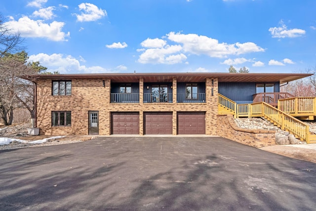 view of front facade with brick siding, aphalt driveway, stairway, a balcony, and an attached garage