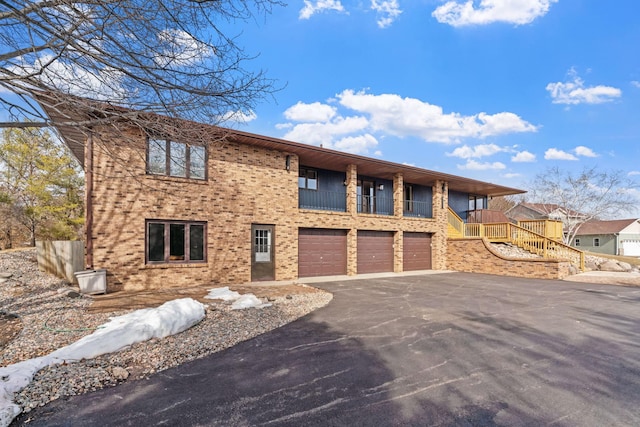 view of front of property with driveway, a balcony, an attached garage, brick siding, and stairs