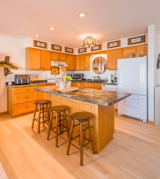 kitchen featuring light wood-style flooring, under cabinet range hood, a kitchen island, white appliances, and a breakfast bar area