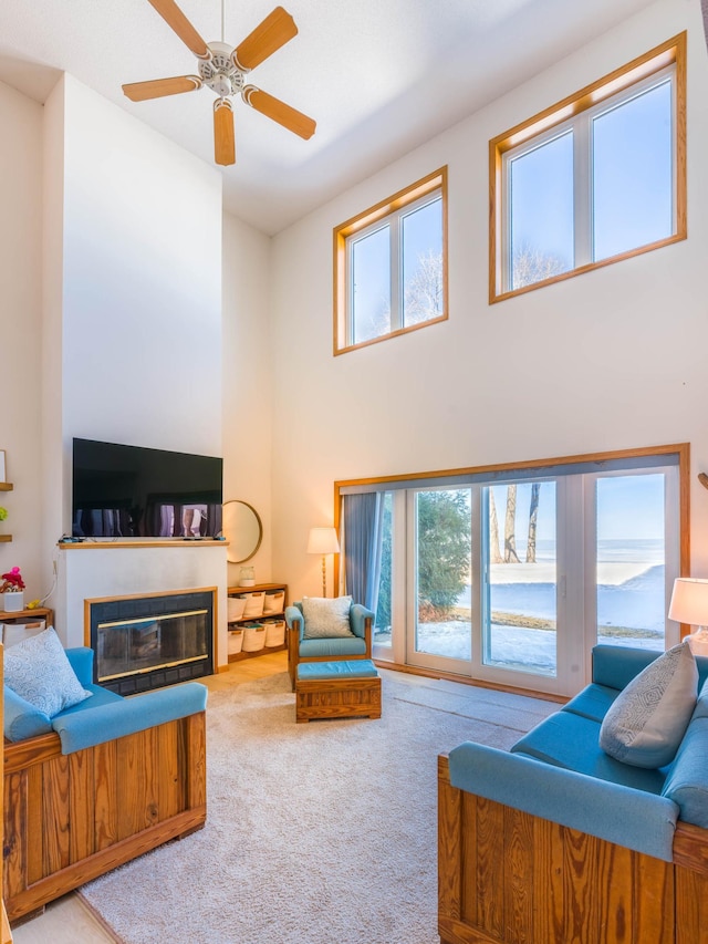 carpeted living room with a glass covered fireplace, a high ceiling, and a ceiling fan