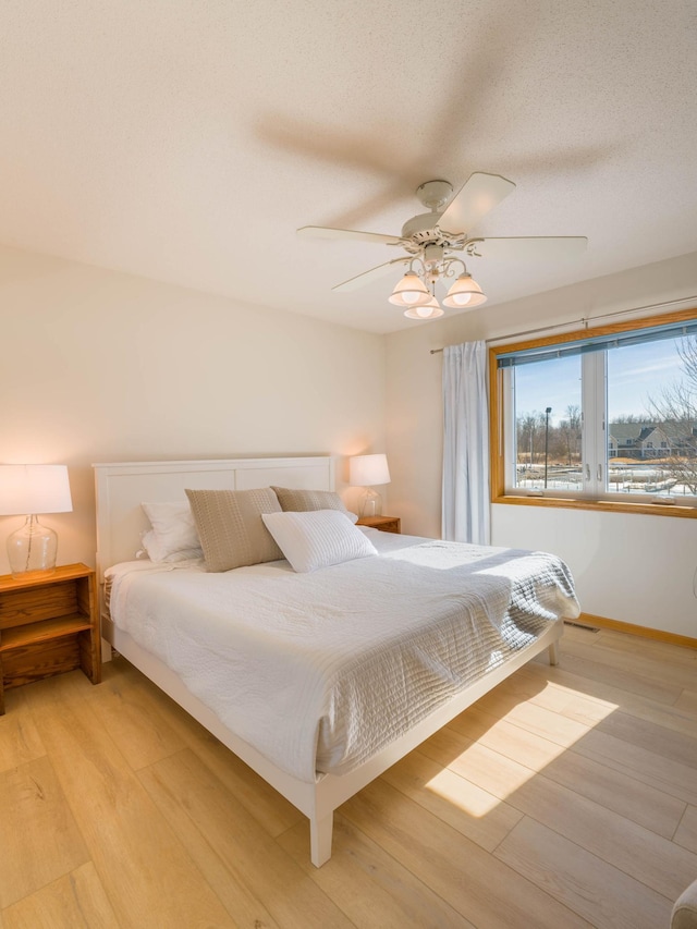 bedroom featuring light wood-type flooring, a textured ceiling, visible vents, and a ceiling fan