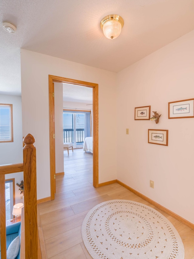 hallway with light wood-type flooring, baseboards, and an upstairs landing