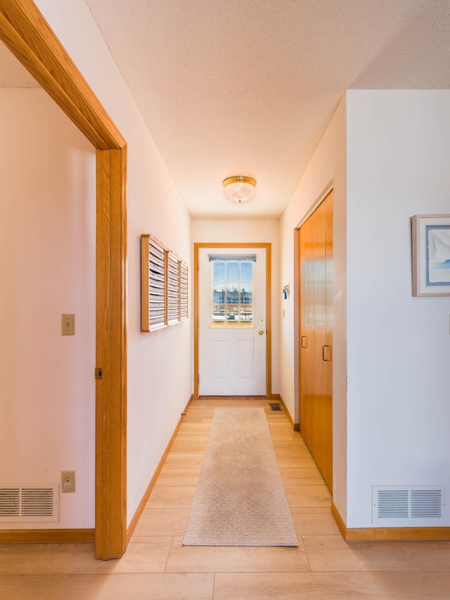 corridor with visible vents, baseboards, light wood-style floors, and a textured ceiling