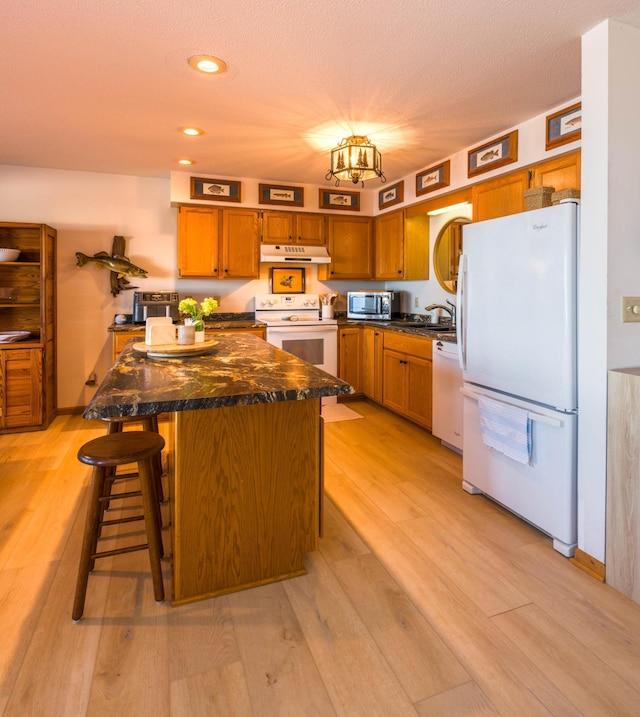 kitchen featuring white appliances, light wood finished floors, under cabinet range hood, and a sink